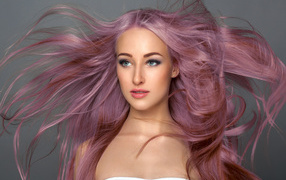 Ветер развивает розовые волосы девушки на сером фоне