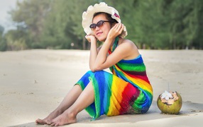 Молодая азиатка сидит на берегу с кокосом