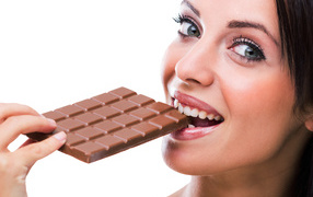 Молодая девушка кусает молочную шоколадку на белом фоне