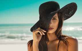 Молодая девушка в черной шляпе на берегу моря