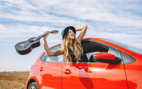 Молодая девушка с гитарой в красной машине летом