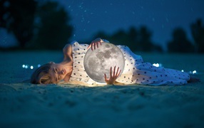 Молодая девушка с луной в руках лежит на песке
