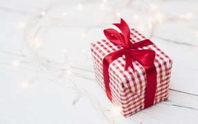 Подарок с красной лентой лежит на столе с гирляндой 