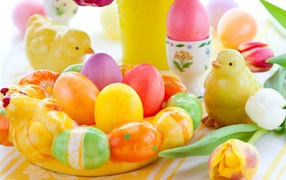 Разноцветные яйца с фигурками на столе с тюльпанами к Пасхе