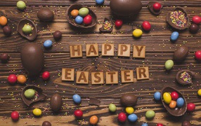 Надпись на английском Счастливой Пасхи на столе с шоколадными яйцами и конфетами