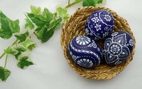 Три раскрашенных яйца в корзинке на столе с веткой 