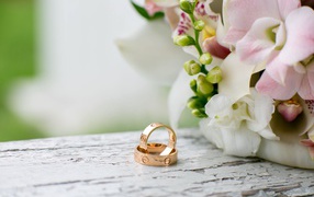 Two gold wedding rings are on the table with flowers.