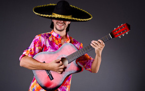 Мужчина в сомбреро с гитарой в руках на сером фоне