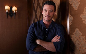 Актер Люк Эванс в рубашке стоит у стены