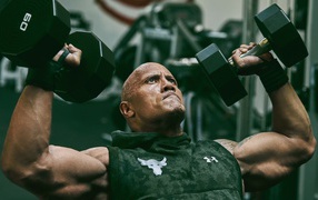 Американский актер, сильный мужчина Дуэйн Джонсон с гантелями в спортзале