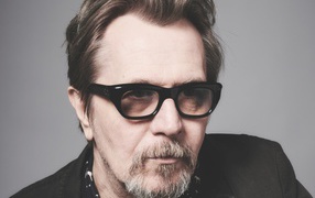 Английский актер Гэри Олдмен в очках на сером фоне