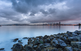 Камни на берегу реки на фоне города под пасмурным небом