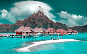 Дома на сваях в голубом океане на фоне горы под белыми облаками