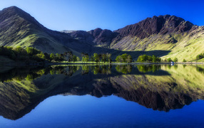 Черные высокие горы с голубым небом отражаются в воде озера