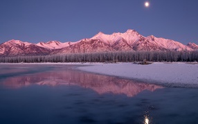 Луна над заснеженными горами отражается в заледеневшем озере 