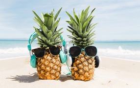 Two pineapples on the beach in sunglasses and headphones