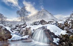 A waterfall flows down from stones against a snow-capped mountain