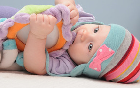 Младенец в шапке грызет мягкую игрушку