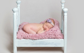 Милый грудной ребенок спит в маленькой кроватке на сером фоне