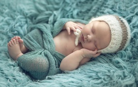 Маленький ребенок в вязаной шапке спит на меховом покрывале