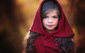 Маленькая красивая голубоглазая девочка с красным капюшоном на голове
