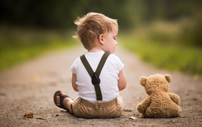 Маленький мальчик сидит на дороге с игрушечным мишкой