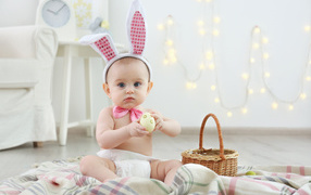 Маленький маленький с ушками зайчика и пасхальным яйцом в руках