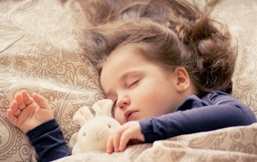 Маленькая милая спящая девочка с игрушкой под одеялом