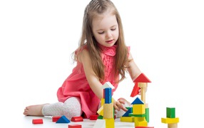 Маленькая девочка строит домик из кубиков на белом фоне