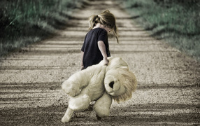 Маленькая девочка несет большую игрушку по дороге 