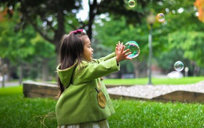 Little girl catches soap bubbles on green grass