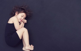 Little girl in a black dress is sleeping on a black background