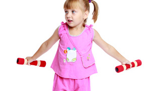 Little girl in a pink suit with dumbbells in her hands on a white background