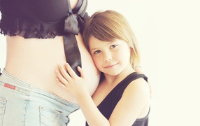 Маленькая девочка прислоняется к животу беременной женщины