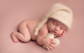 Маленький спящий ребенок в теплой шапке на розовом фоне
