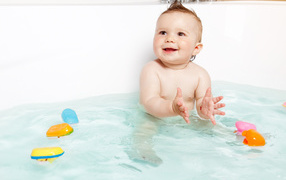 Маленький улыбающийся ребенок с игрушками в ванной 