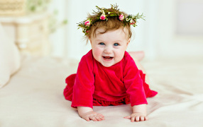 Маленькая улыбающаяся девочка в красном платье с венком на голове