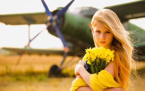 Long-haired girl with a bouquet of yellow chrysanthemums on the background of an airplane