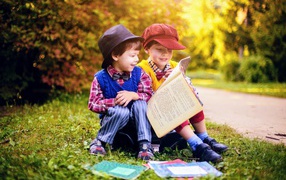 Два маленьких мальчика читают книгу сидя на траве