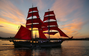 Big ship with red sails on sunset background