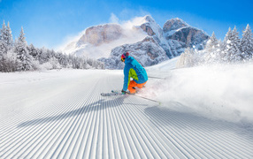 The skier goes down the slope against the backdrop of snow-capped mountains