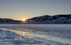 Покрытая льдом река у заснеженного леса на рассвете 