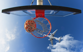 A plane flies over a basketball hoop in the blue sky