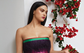 Actress Camila Mendes stands against a wall with flowers