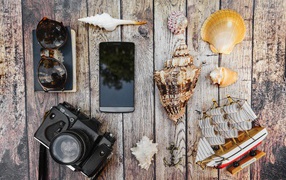 Фотоаппарат, смартфон, ракушки, очки и паспорт на столе