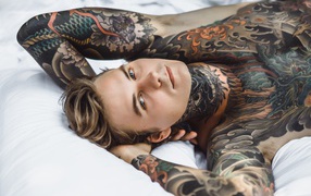 Handsome young man with tattoos on his body is lying on the bed