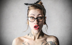Удивленная девушка в очках с татуировками на теле