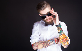 The man in glasses with tattoos on his hands on a gray background