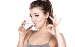 Молодая спортивная девушка пьет воду из стакана