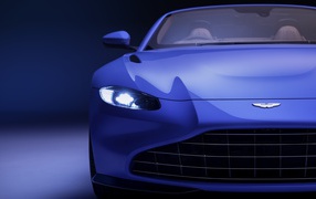 Синий автомобиль Aston Martin Vantage Roadster 2020 года с включенной фарой 